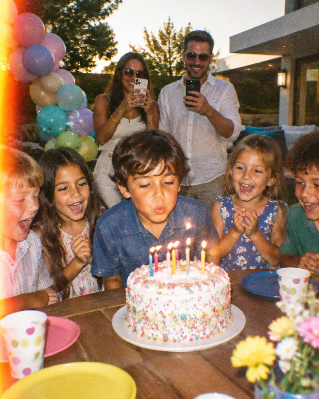 Kids around a birthday cake while parents take photos