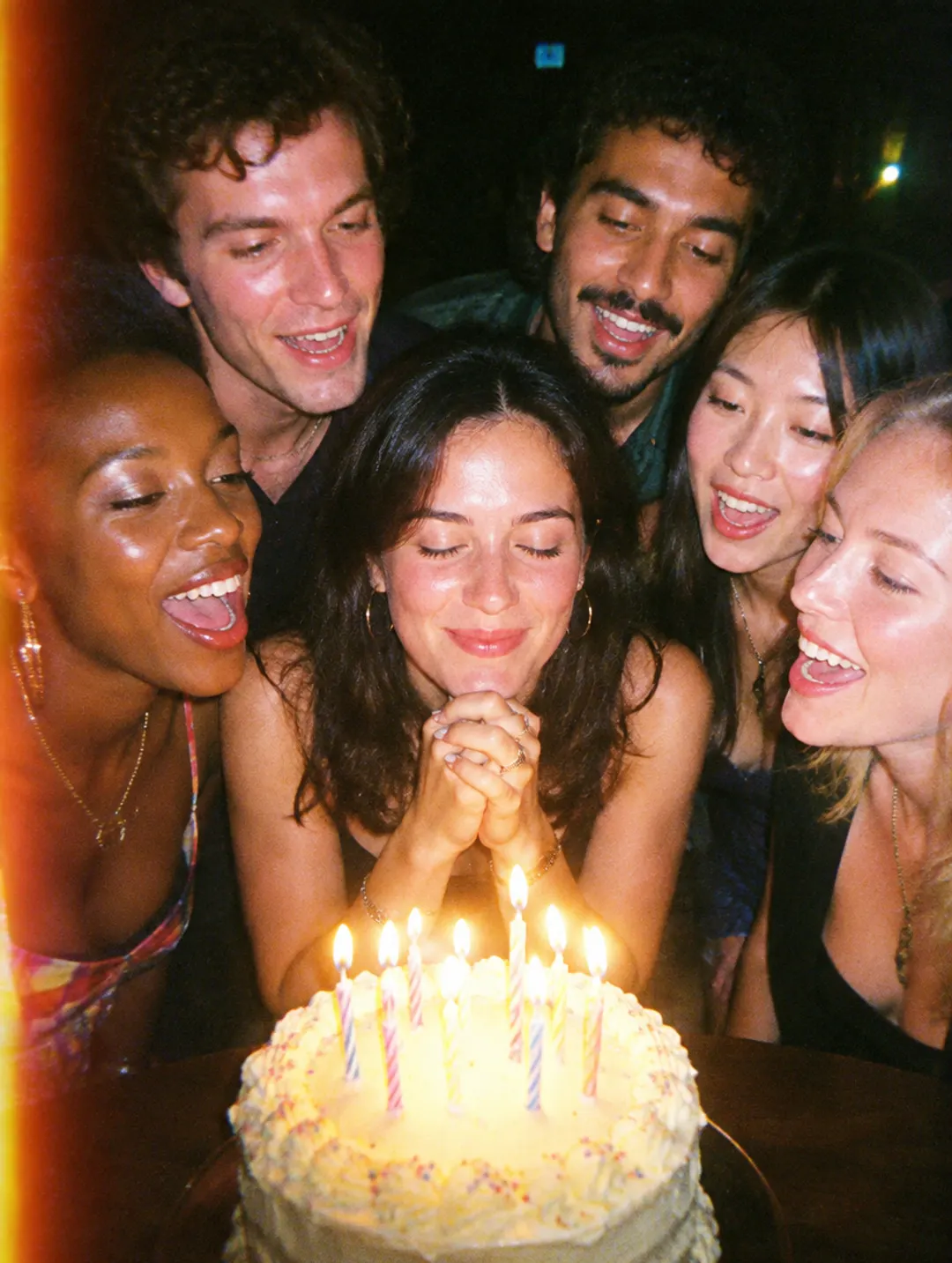 Friends cheering as a woman makes a wish over her birthday cake