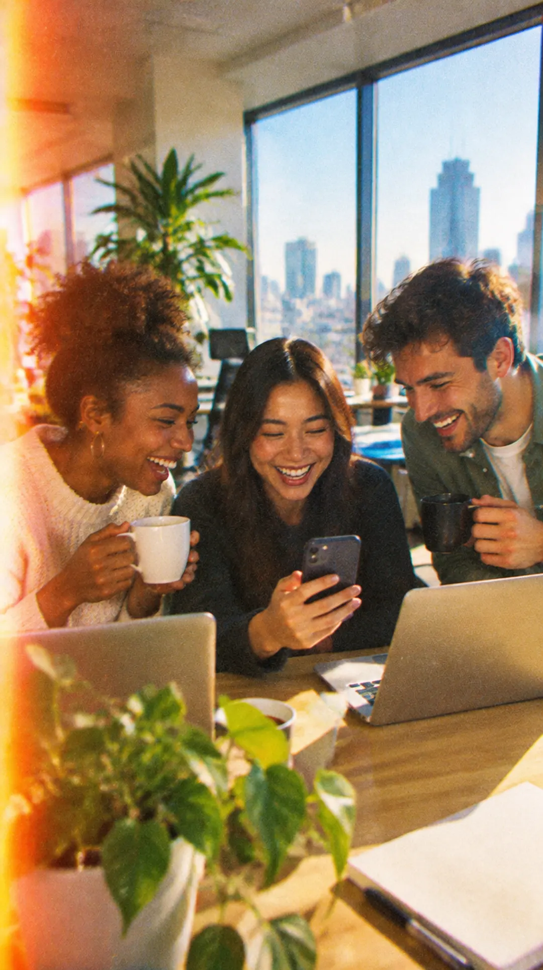 Coworkers laughing at party photos on a phone at the office